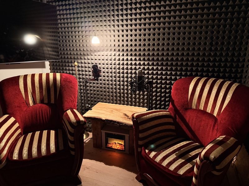 Podcast studio: two red armchairs, an electric fireplace and two microphones on boom arms
